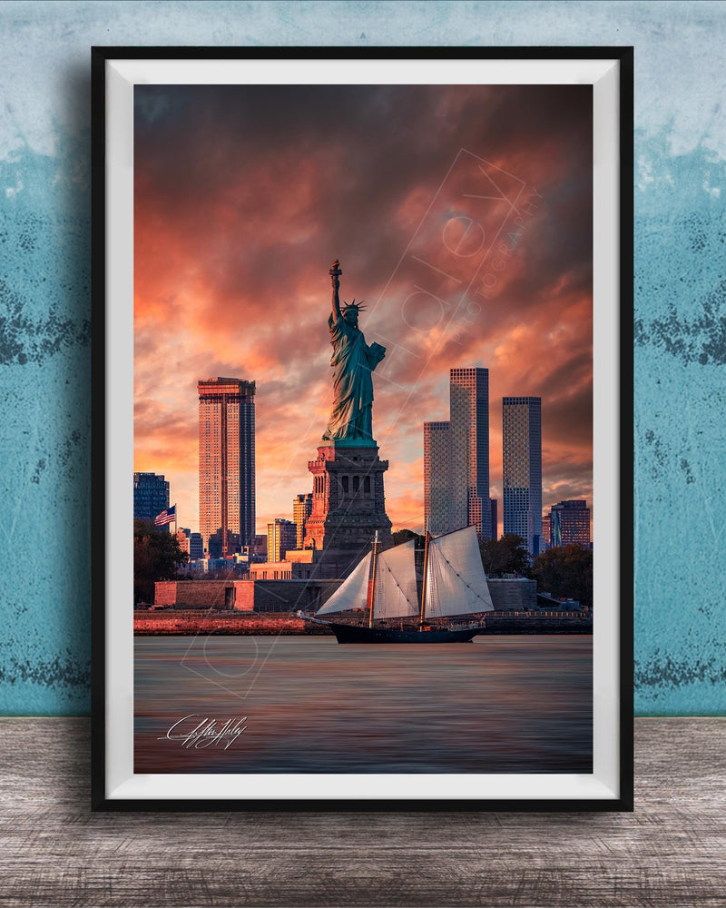 a framed photograph of the Statue of Liberty in New York City, with the city skyline in the background and a sailboat in the foreground.
