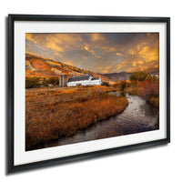 a picturesque rural landscape with a farmhouse nestled among rolling hills and a winding stream. The sky is filled with vibrant orange and yellow clouds, creating a warm and inviting atmosphere. The overall scene is serene and peaceful, showcasing the beauty of nature and the tranquility of the countryside.