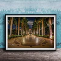 A framed photograph depicting a serene nighttime scene of a palm-lined walkway with a circular pattern, illuminated by warm lighting.