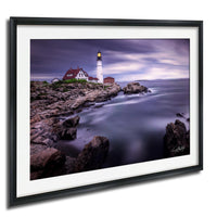 A framed photograph depicting a lighthouse on a rocky shore, with the ocean in the background.