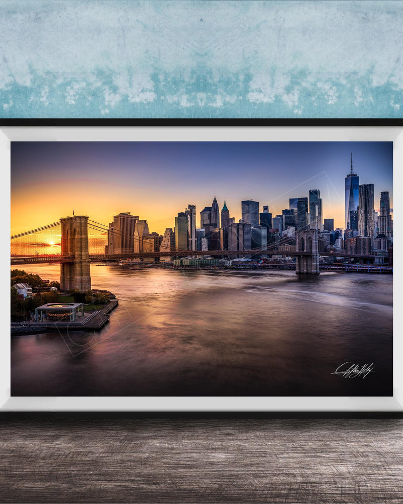 A framed photograph of the skyline of New York City at sunset, with the Brooklyn Bridge and other skyscrapers visible in the background.