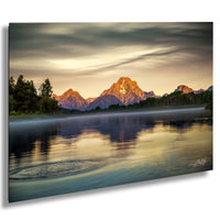 a serene landscape with a mountain range in the background, its peaks illuminated by the warm glow of the setting sun. The mountains are reflected in a calm lake, creating a mirror-like effect on the water's surface. The sky above is filled with clouds, adding depth and texture to the scene. The overall composition is balanced and harmonious, with the mountains and lake as the focal points.