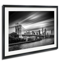 A black and white photograph of the Brooklyn Bridge and the New York City skyline, with the bridge spanning across the frame and the city's skyscrapers visible in the background.