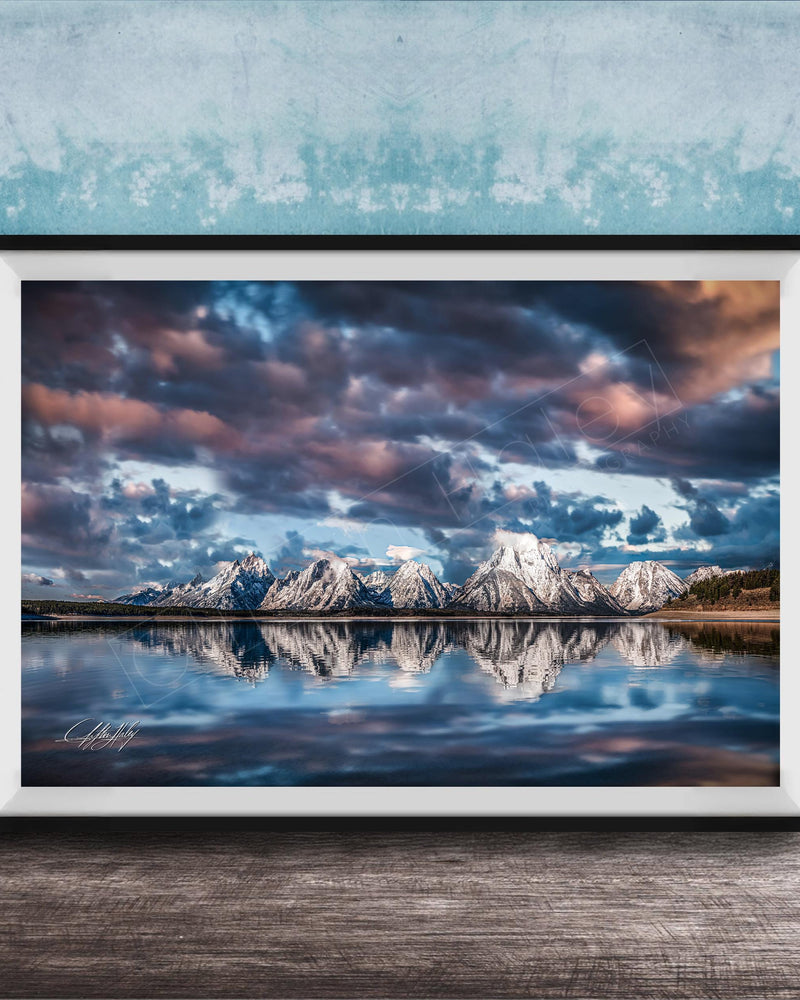 A framed photograph of a serene landscape with snow-capped mountains reflected in a calm lake, set against a dramatic sky with clouds.