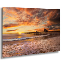 a serene beach scene at sunset, with a wooden pier extending into the calm waters. The sky is filled with vibrant orange and pink hues, creating a stunning backdrop for the tranquil setting.