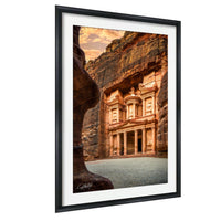 a large, ancient stone structure carved into a cliff face, with a warm, golden glow from the setting sun illuminating the scene.