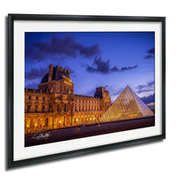 the Louvre Museum in Paris, France, with its iconic glass pyramid structure illuminated against a dark blue sky.