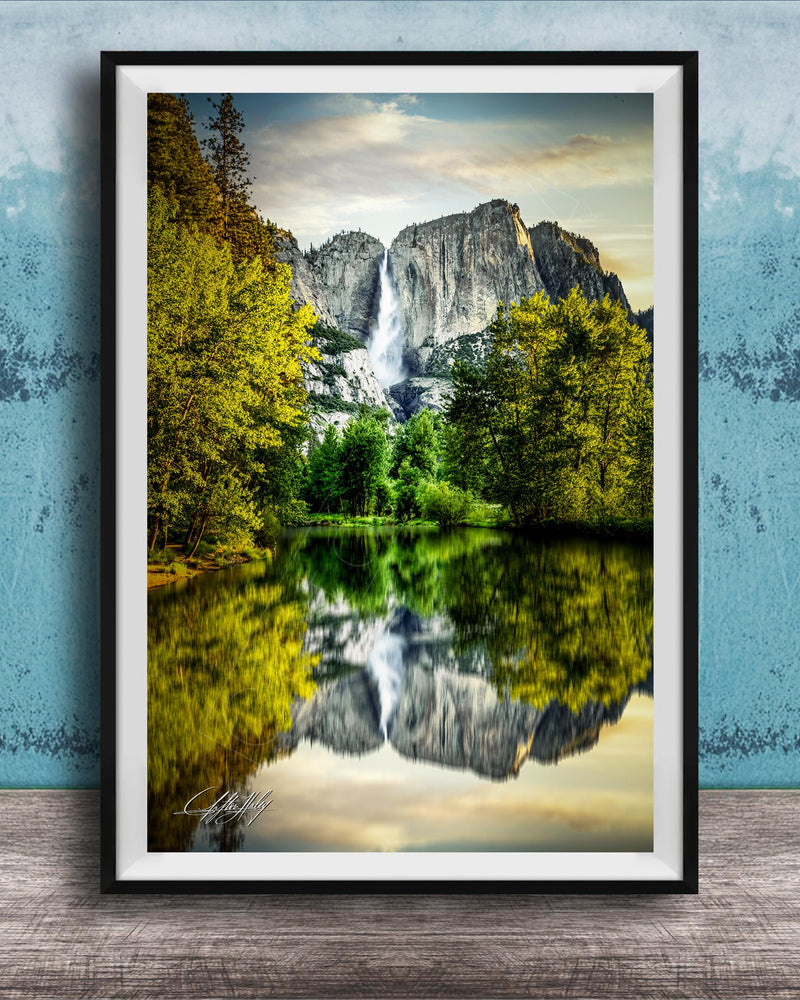 A framed photograph of a serene landscape with a waterfall cascading down a rocky cliff, surrounded by lush green trees and reflected in a calm lake below.