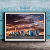 A framed photograph of the New York City skyline at sunset, with the city's skyscrapers silhouetted against a dramatic sky filled with clouds and vibrant colors.
