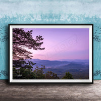 A framed photograph of a scenic mountain landscape at sunset, with a silhouetted tree in the foreground and a hazy, purple sky in the background.