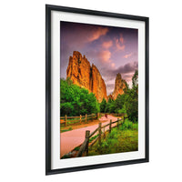 a scenic landscape with towering red rock formations against a vibrant sky, surrounded by lush greenery and a winding path.