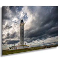 A white lighthouse with a black top stands tall against a dramatic cloudy sky, with a grassy field in the foreground.