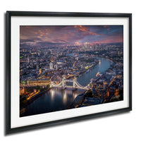 The image is a framed aerial view of a city at night, showcasing a river with a bridge and the city skyline in the background.