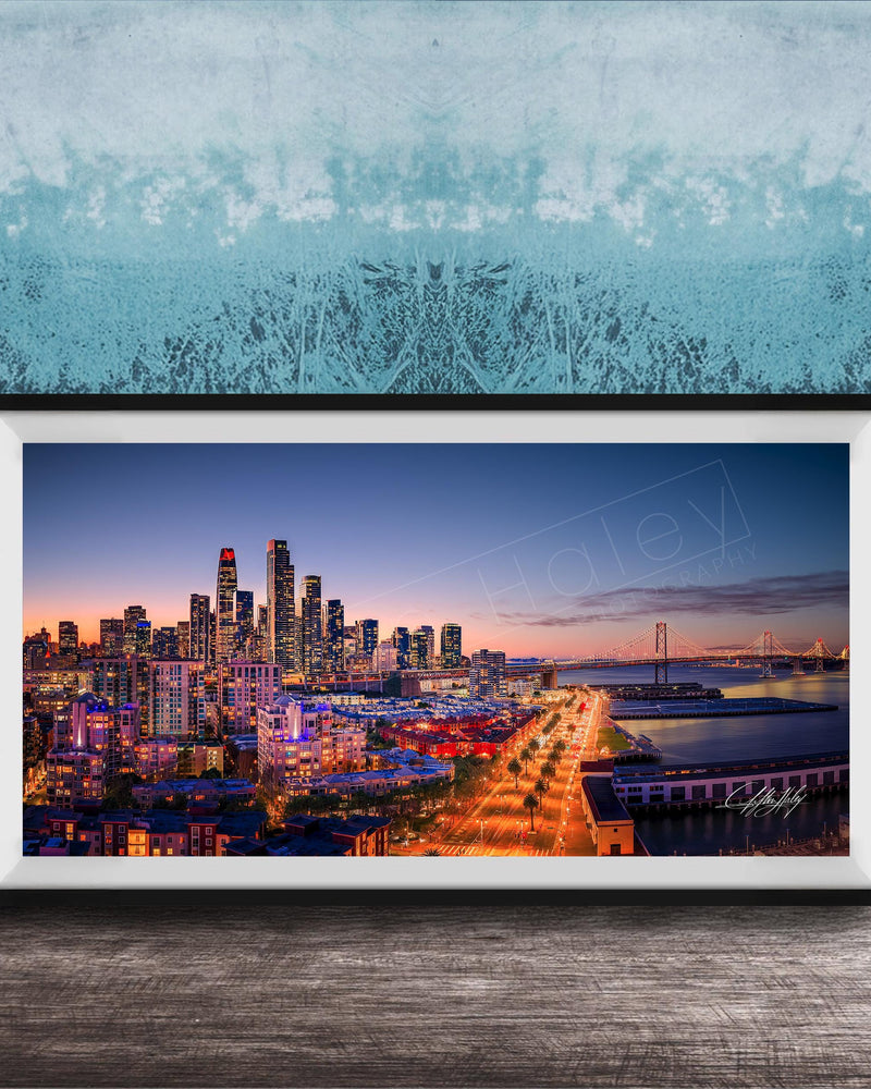 A framed photograph of a city skyline at dusk, with the city lights illuminating the buildings and the water in the background.