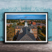 The image is a framed aerial view of a city, showcasing a mix of buildings, trees, and a prominent clock tower.