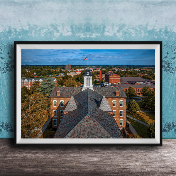 The image is a framed aerial view of a city, showcasing a mix of buildings, trees, and a prominent clock tower.