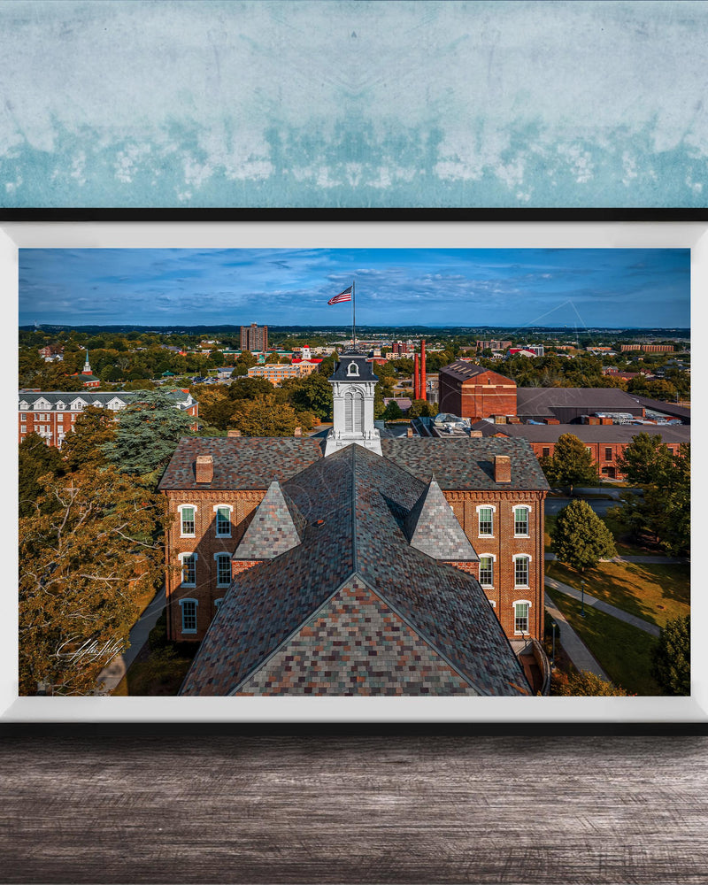 The image is a framed aerial view of a city, showcasing a mix of buildings, trees, and a prominent clock tower.