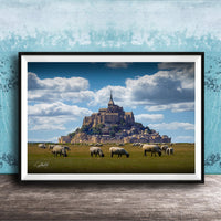 A framed photograph depicting a pastoral scene with a large castle or hill in the background, surrounded by a grassy field where a herd of sheep are grazing.