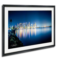 A framed photograph depicting a city skyline at night, with the city lights reflected in the water below.