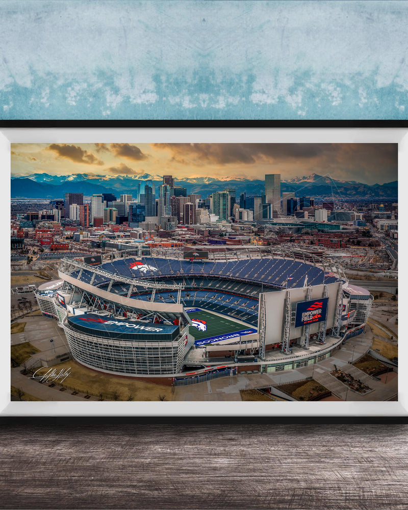 The image is an aerial view of a large sports stadium, likely a football stadium, with the city skyline in the background.