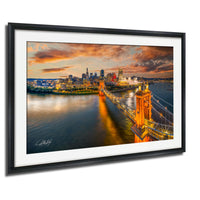 A framed photograph depicting the Cincinnati skyline at sunset, with the city's iconic bridges illuminated against a vibrant sky.