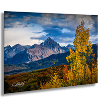 a breathtaking mountain landscape with snow-capped peaks, a vibrant mix of autumn foliage, and a dramatic cloudy sky.