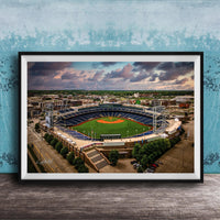 An aerial view of a baseball stadium with a lush green field, surrounded by buildings and a cloudy sky.