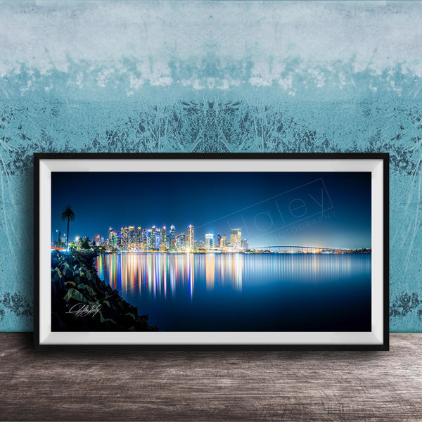 A framed photograph of a city skyline at night, with the city's lights reflected in the water below.