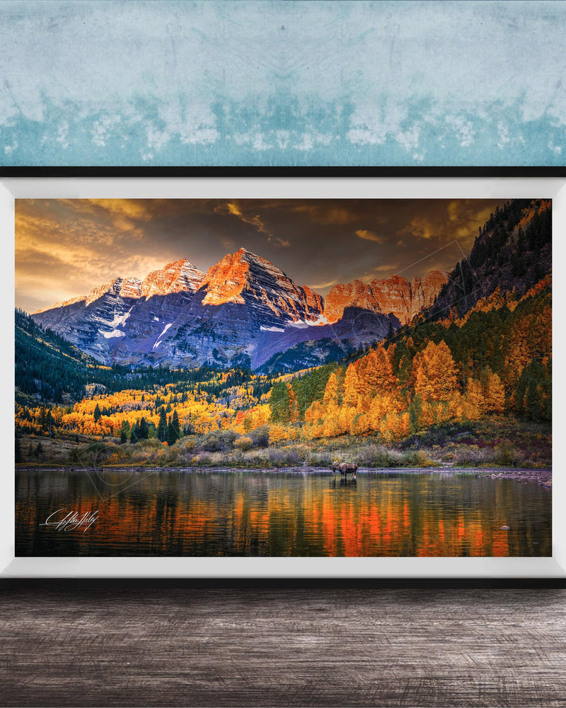 The image is a framed photograph depicting a scenic mountain landscape with a lake in the foreground, surrounded by trees with autumn foliage.