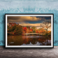 A framed photograph depicting a scenic autumn landscape with a bridge, trees, and a body of water reflecting the vibrant colors of the season.