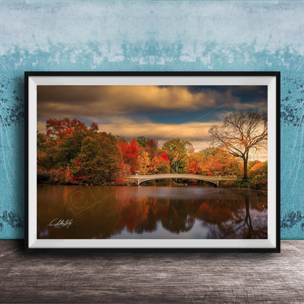 A framed photograph depicting a scenic autumn landscape with a bridge, trees, and a body of water reflecting the vibrant colors of the season.