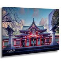 A traditional Japanese temple with a red and white exterior, surrounded by trees and a modern building in the background.