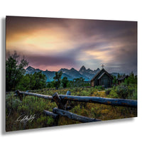 a serene rural landscape with a wooden fence, a small wooden building, and a mountain range in the background, all bathed in the warm glow of a colorful sunset.