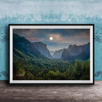 The image is a framed photograph of a mountainous landscape with a full moon in the sky, surrounded by trees and forests.