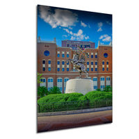 a large statue of a man on a horse in front of a brick building, with a blue sky and clouds in the background.