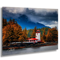 A picturesque lighthouse stands on a rocky shore, surrounded by a forest of autumn-colored trees and a dramatic cloudy sky.