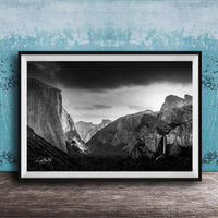 A black and white photograph of a mountainous landscape, with dramatic clouds and a waterfall in the foreground.
