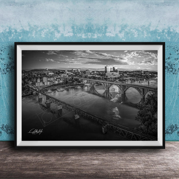 A black and white aerial photograph of a cityscape with a large bridge spanning a river, set against a blue textured wall.