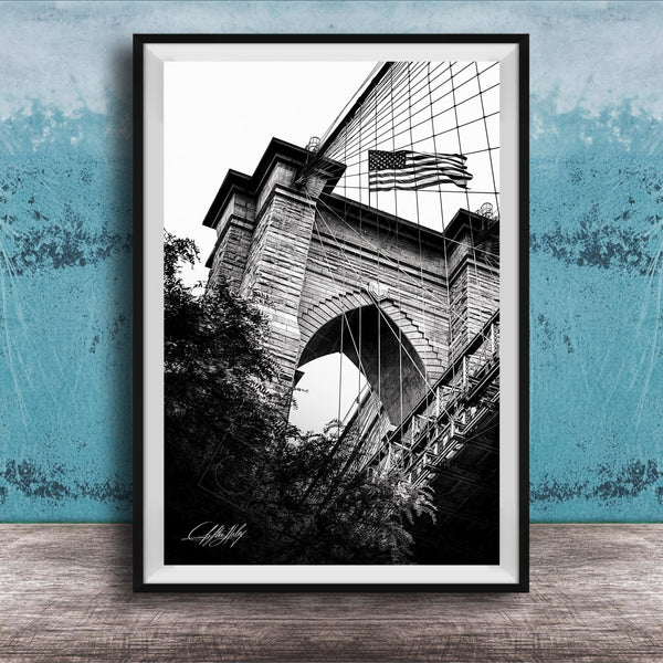 A black and white photograph of a brick bridge with an American flag flying above it, set against a blue textured background.