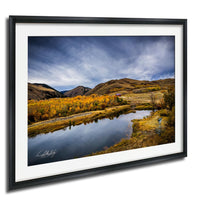 a serene landscape with a calm river reflecting the surrounding mountains and trees. The sky is filled with clouds, creating a picturesque and tranquil atmosphere.