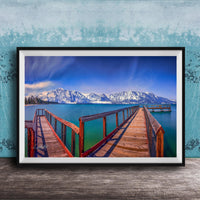A framed photograph of a wooden pier extending into a serene lake, with snow-capped mountains in the background.