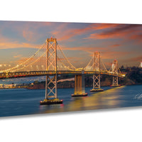 a large suspension bridge spanning a body of water, with its lights illuminated against a colorful sunset sky.