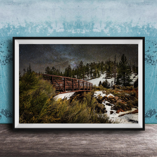 A framed photograph depicting a wooden bridge crossing a snowy mountain landscape at night, with a starry sky overhead.