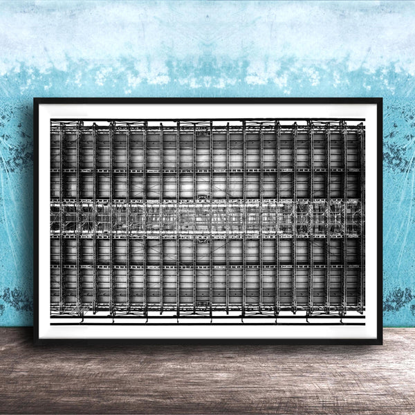 The image is a framed black and white photograph of a grid-like structure, possibly a building or a machine, set against a blue textured wall.
