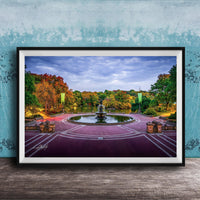 A framed photograph of a park with a fountain, surrounded by trees with autumn foliage, set against a blue wall.