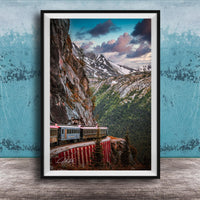 A framed photograph depicting a train traveling along a winding track that runs along the side of a steep, rocky mountain.