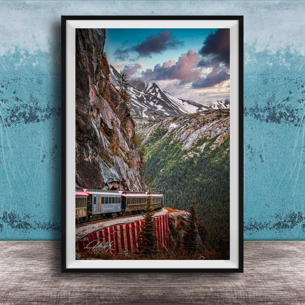A framed photograph depicting a train traveling along a winding track that runs along the side of a steep, rocky mountain.