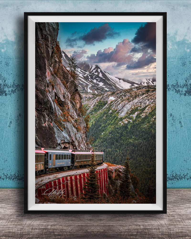 A framed photograph depicting a train traveling along a winding track that runs along the side of a steep, rocky mountain.