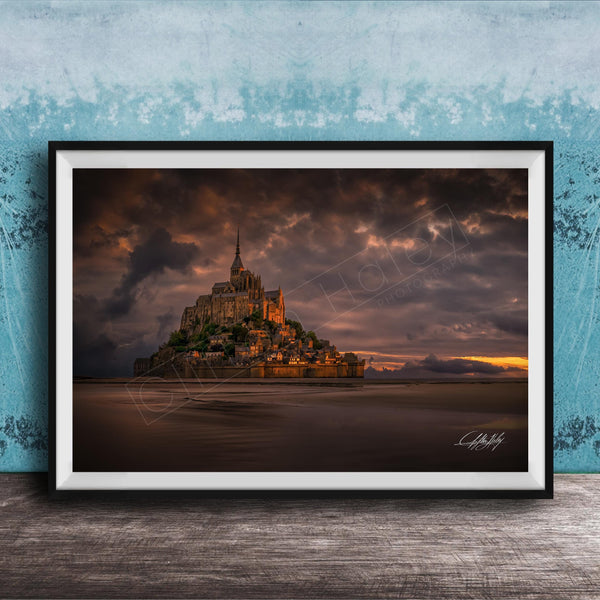 A framed photograph of the iconic Mont Saint-Michel in Normandy, France, with a dramatic sky in the background.