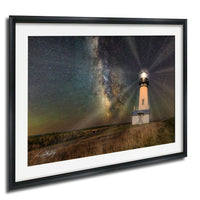 A framed photograph depicting a lighthouse standing in a field at night, with a starry sky and a glowing milky way galaxy in the background.